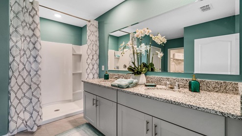 Bathroom featuring granite countertops, a sizeable wall mirror, and ample cabinetry, along with a walk-in shower.