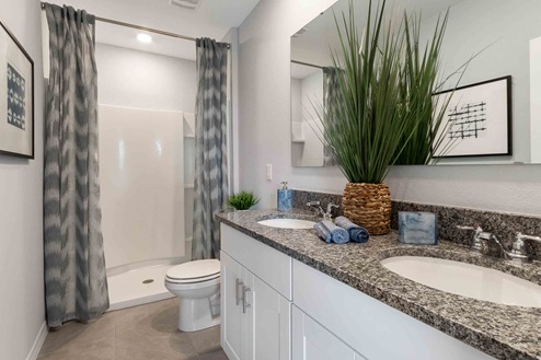 Bathroom featuring granite countertops, a sizeable wall mirror, and ample cabinetry, along with toilet and a walk-in shower.