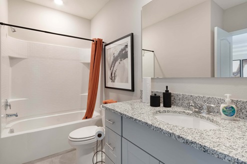 Single vanity bathroom with granite countertop, large wall mirror, toilet and shower.