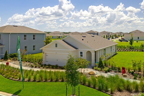 Arial view of single story new home with driveway, large windows, and grassy front yard.